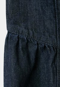 Tissu en denim bleu foncé avec un détail de couture froncée créant une texture froissée et un motif de tissage diagonal visible.