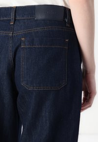 Mørke denim jeans med en glatt tekstur, med kontraststing og et lappemerke i midjen. Inkluderer baklommer.