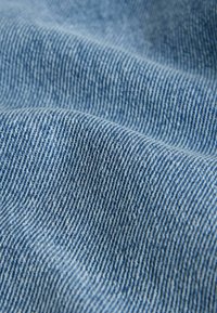 Blauer Denimstoff mit sichtbaren weißen Schussfäden, glatter Textur, leichtem Gewicht und einem dezenten Rippenmuster, das durch gewebte Fäden entsteht.