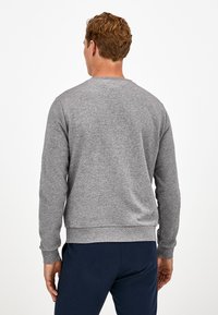 Sudadera gris de manga larga, cuello redondo y puños acanalados. Tejido de algodón suave con un acabado texturizado. Combinada con pantalones azul marino.