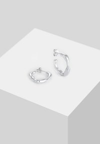 Sølvøreringe med en organisk, bølget design. Den polerede finish fremhæver den glatte tekstur og den uregelmæssige form. Inkluderer stud bags.