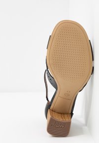 Semelle d'une sandale à talon noire avec une bande de roulement beige, talon bloc en bois et semelle en caoutchouc antidérapante, taille 37 visible sur la semelle.