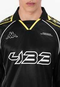 Fekete sportmez sárga gallérral és díszítésekkel, fehér "433" felirattal és Kappa logóval a mellrészen. Sima textúra.
