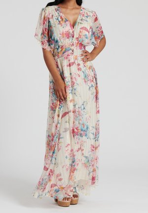 Donna che indossa un lungo vestito floreale e fluente con maniche corte a sbuffo e bottoni davanti, abbinato a sandali platform.