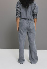 Grå denim outfit bestående af en løstsiddende jakke med opsmøgede ærmer og højtaljede, brede bukser med baglomme-detalje.