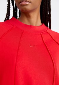 Red sweatshirt featuring a textured design, ribbed neckline, and tonal Nike logo. Close-up shows stitching details and fabric consistency.
