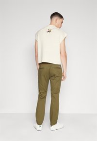 Top senza maniche lavorato a maglia color crema con un logo sulla schiena, abbinato a pantaloni affusolati verde oliva e sneakers bianche. Design semplice e casual.