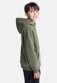 Khaki zielona bluza z sztruksu z kieszenią z przodu i dużym kapturem, z prążkowaną teksturą i luźnym krojem. Czarne spodnie dopełniają stylizację.
