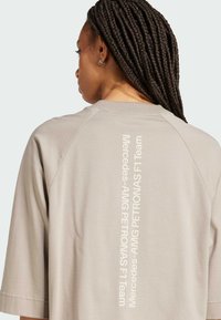 Světle šedé oversized tričko s kulatým výstřihem a krátkými rukávy. Na zadní straně je vertikální bílý text: „Mercedes-AMG PETRONAS F1 Team“. 