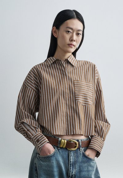 Braun-weiß gestreiftes Langarmshirt mit Tasche, hohem Kragen und weiter Passform, kombiniert mit hoch taillierten hellblauen Jeans und einem braunen Gürtel.