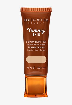 Braune Tube mit metallisch orangefarbenen Akzenten, beschriftet mit "Yummy Skin Serum Skin Tint." Enthält 45 ml getöntes Serum. Glatte Oberfläche, Pumpspender.