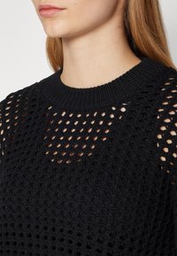 Schwarzer gestrickter Pullover mit strukturiertem, offenem Webmuster, Rundhalsausschnitt und geripptem Kragen. Hervorzuheben ist das anspruchsvolle Muster und das leichte Erscheinungsbild.