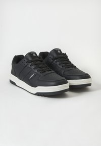 Adidași negri din piele cu o talpă intermediară albă, vârf rotund, suprafață texturată și șireturi negre. Prezintă logo pe limbă și pe părțile laterale.