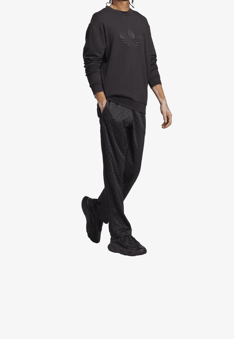 Svart sweatshirt med texturerad logotyp, kombinerad med svarta mönstrade joggare och svarta sportskor. Slät tyg och avslappnad passform.