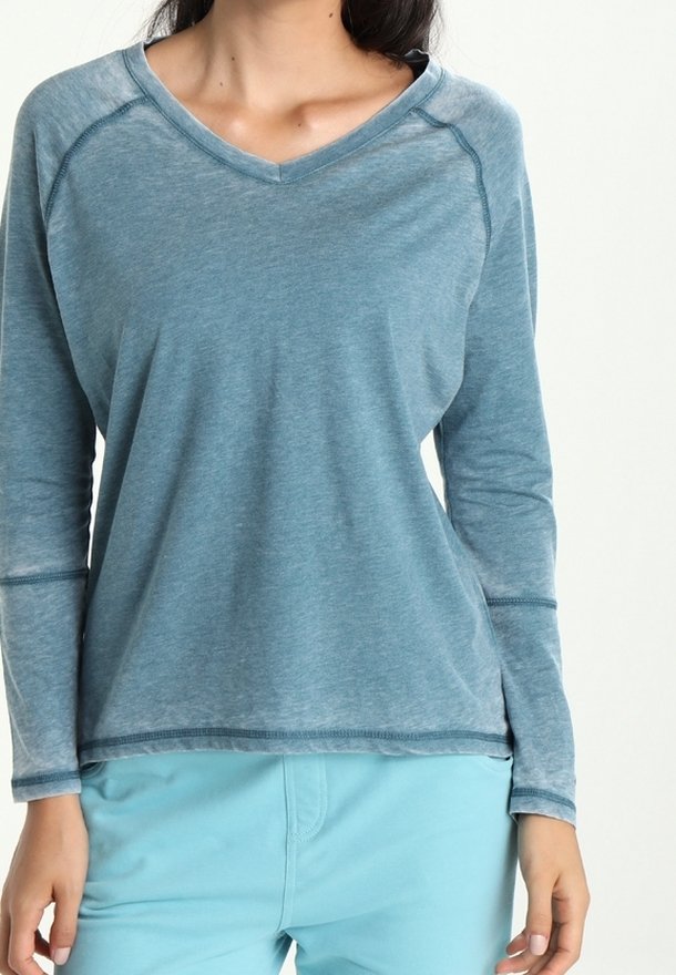 Koszulka z długim rękawem i dekoltem w serek, wykonana z miękkiego, lekkiego niebieskiego materiału. Posiada swobodny krój z szwami raglanowymi i przeszyciami dekoracyjnymi.