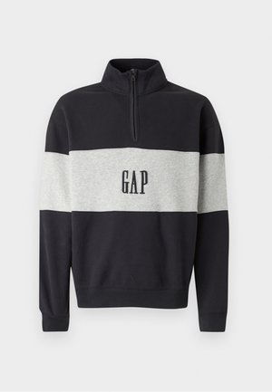 Črna in siva sweatshirt z delnim zadrgo na ovratniku in črnim logotipom "GAP". Ima barvno blokirano zasnovo z mehkobo in teksturirano tkanino.