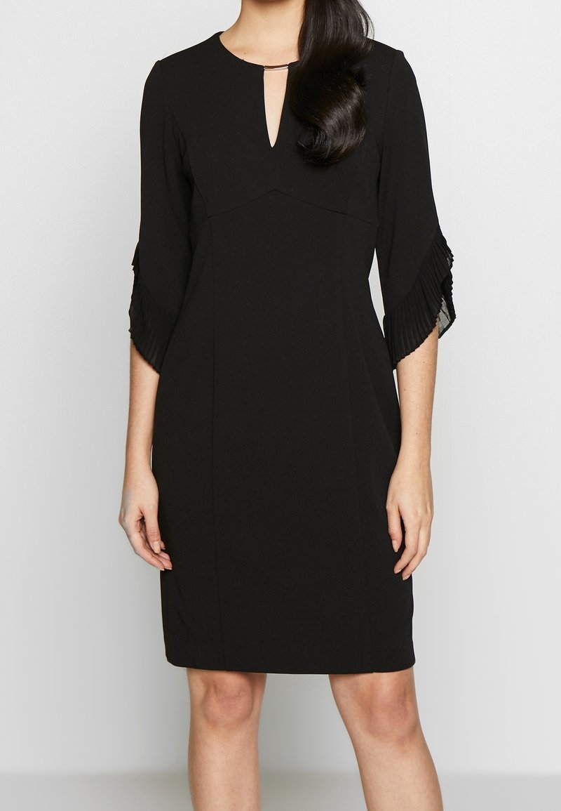 Svart klänning med trekvartslånga veckade ärmar, nyckelhålsutringning, slät tyg. Rak skärning med minimal detaljering, lämplig för formella tillfällen.