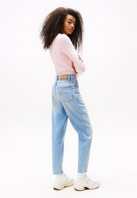 Light pink knitted sweater with a cable design, high-waisted light blue jeans, and white sneakers with gray accents. Back view.