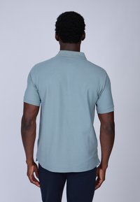 Polo shirt bleu clair avec un col et des manches courtes, arborant une texture lisse et un motif de tissage subtil et uniforme. Vue de dos présentée.