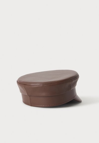 Casquette plate en cuir marron avec une courte visière incurvée, posée sur une surface blanche.