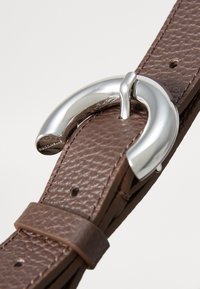 Ceinture en cuir marron avec une surface texturée, dotée d'une boucle en métal argenté brillant de forme ronde et d'une sangle en cuir avec des détails de couture.