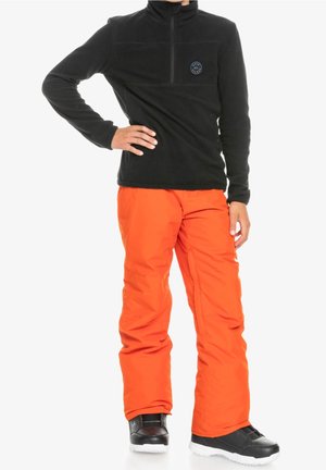 Sudadera negra de vellón con cremallera hasta el pecho y un logo azul, combinada con pantalones impermeables de nieve de color naranja brillante y zapatos de invierno negros.