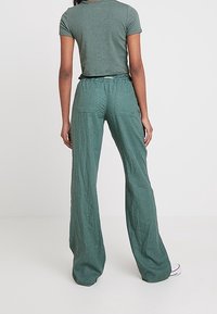 Groene geribde shirt gecombineerd met hoge taille, losvallende groene broek. De broek heeft een gestructureerde stof en opgestikte zakken aan de achterkant.