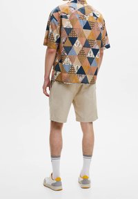 Camisa de manga corta con un patrón de triángulos multicolores en tonos marrones, azules y crema, combinada con pantalones cortos beige y calcetines blancos.