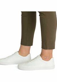 Hvide lærreds sneakers med en glat overflade og rund tå. Sammen med olivengrønne tætsiddende bukser, der viser et ankelarmbånd.