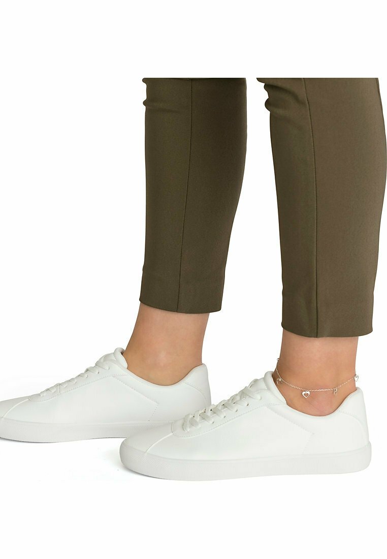 Hvide lærreds sneakers med en glat overflade og rund tå. Sammen med olivengrønne tætsiddende bukser, der viser et ankelarmbånd.