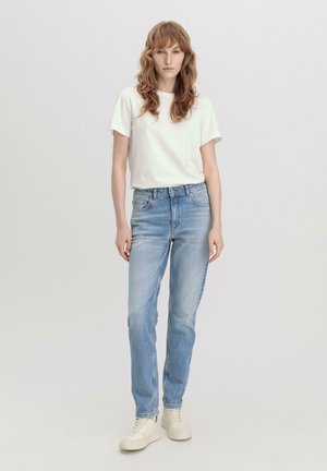 Weißes T-Shirt mit kurzen Ärmeln kombiniert mit hellblauen, geraden Jeans. Das Outfit hat eine lässige Passform und beiger Sneaker.