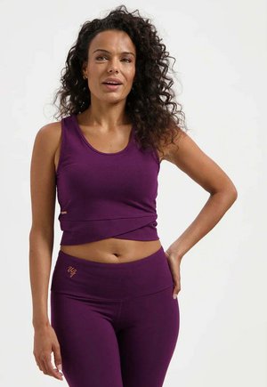 Paarse cropped tanktop met een ronde halslijn, gecombineerd met paarse, hooggetailleerde leggings. Beide items hebben een gladde textuur en een minimalistisch design.