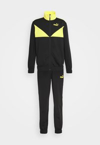Survêtement Puma noir et jaune avec veste zippée dotée d’un chevron jaune et pantalon assorti avec logo Puma sur la cuisse.