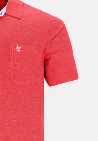 Röd kortärmad skjorta med en texturerad tyg, som har en bröstficka och en liten logotypdetalj på fickan.