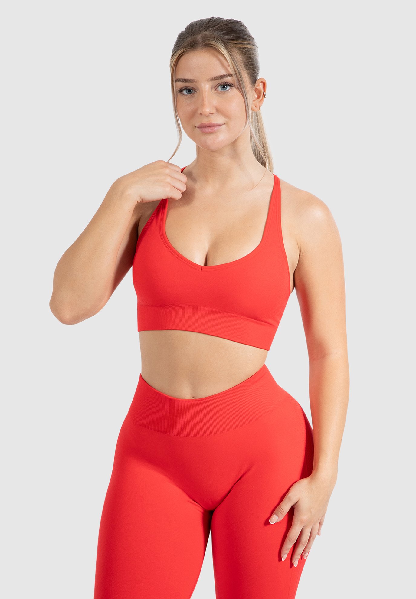 Red sports bra and high-waisted leggings made of stretchy fabric. The bra features a scoop neck and thin straps. The outfit has a smooth texture.