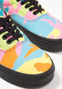 Paire de baskets avec des lacets noirs, des semelles noires, et des motifs abstraits colorés en orange, jaune, bleu, rose et vert.