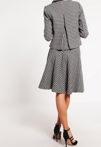 Sada kabátu a sukně s černobílým vzorem houndstooth. Kabát má přiléhavý střih s rozparkem; sukně je rozšířená. Černé lodičky.