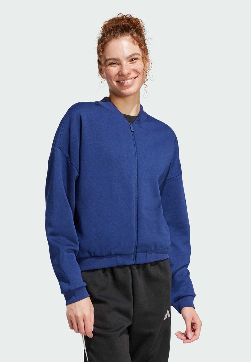 Sudadera azul con cremallera y un corte relajado, con puños y dobladillo de canalé. Hecha de una tela suave, cuenta con un cuello alzado y bolsillos laterales.