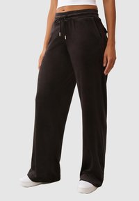 Schwarze Jogginghosen aus weichem Stoff, mit einem Kordelzugbund, seitlichen Taschen und einem lockeren Schnitt. Kombiniert mit weißen Sneakern.