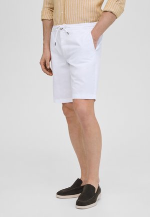 Shorts en coton blancs avec une taille élastique, un cordon de serrage, des poches latérales et des revers, associés à des chaussures noires à enfiler.