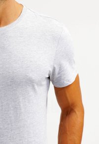 T-shirt in cotone grigio con colletto rotondo, maniche corte e una texture morbida. Cuciture visibili al collo e sulle spalle.