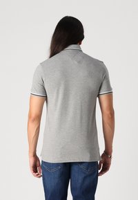 Šedé polo tričko s krátkým rukávem, které má límeček a kontrastní pruhované detaily na lemu rukávů. Tkanina vypadá hladce a přiléhavě.