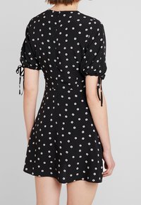 Svart kort klänning med vitt blommönster, puffärmar och banddetaljer. Mjuk tyg, åtsittande midja och lätt utsvängd kjoldesign.