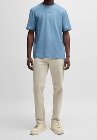 Světle modré bavlněné tričko s kulatým výstřihem a malým logem „BOSS“. Kombinováno s béžovými kalhotami rovného střihu a krémovými teniskami.