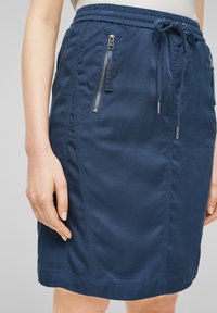 Mörkblå kjol i texturerad tyg med elastisk dragsko i midjan, med två zippered sidofickor och rak passform.