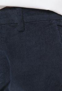 Tessuto in corduroy blu marino con righe verticali, caratterizzato da una vita semplice e una tasca posteriore, con attenzione ai dettagli di texture e colore.