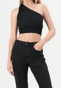 Svart ribbad enaxlad crop top bärs med högmidjade svarta jeans. Toppen har en figurnära design och jämn textur.