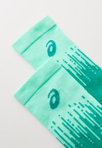 Chaussettes de sport turquoise avec un motif texturé, un effet dégradé progressif et un logo en bleu canard près du haut.