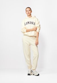 Hoodie w kolorze kremowym z napisem "LAMANIA" oraz dopasowane spodnie dresowe. Oba wykonane z miękkiego materiału, z elastycznymi mankietami i swobodnym krojem.