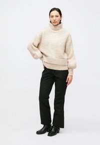 Beige højhalset sweater med ribstrikket tekstur, kombineret med sorte bukser med lige ben og sorte ankelstøvler. Blødt, hyggeligt materiale, afslappet pasform.